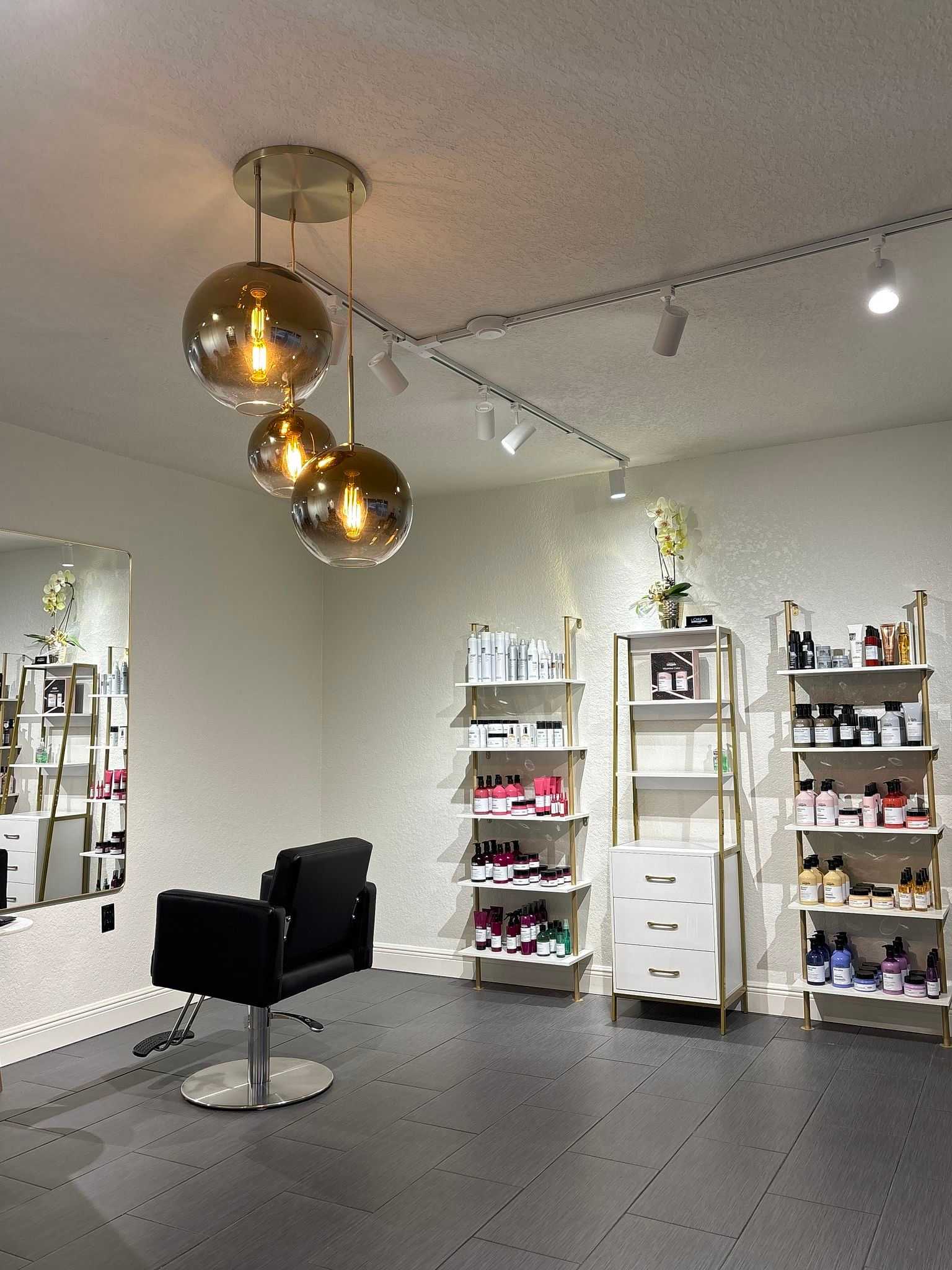 Modern salon with black styling chair, hanging lights, and shelves stocked with beauty products.